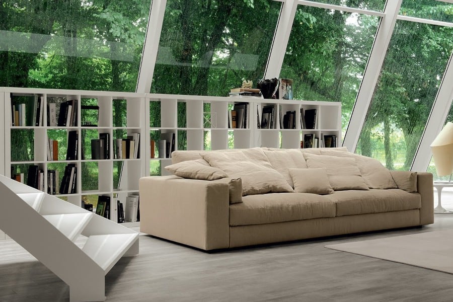 Modernes, beiges Sofa von Alberta in einem schrägen Wintergarten mit Regal dahinter